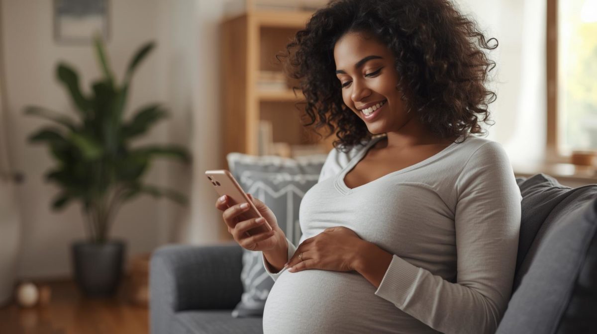 Mulher grávida em casa consultando app gravidez no celular para acompanhar o desenvolvimento do bebê