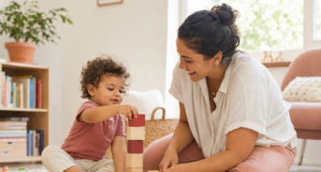 Mãe brinca com criança que empilha blocos de madeira durante uma atividade ligada aos marcos do desenvolvimento infantil.