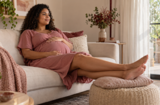 Gestante sentada no sofá com as pernas elevadas e os pés apoiados em uma almofada.