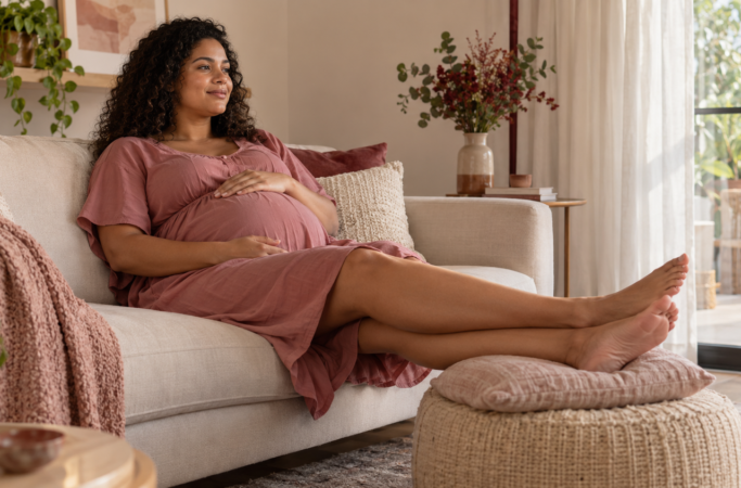 Gestante sentada no sofá com as pernas elevadas e os pés apoiados em uma almofada.